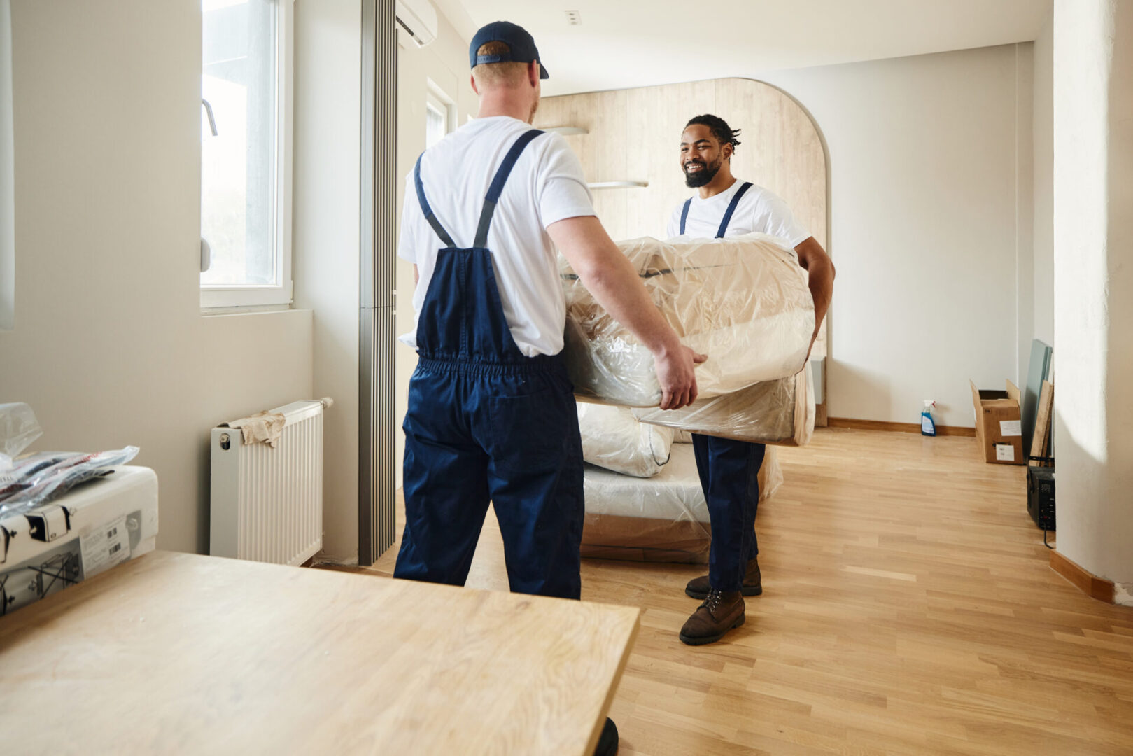 Two movers carrying a sofa through a bright room.